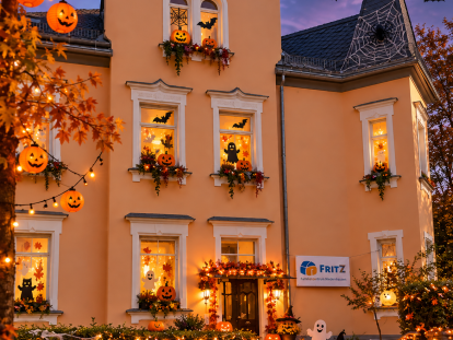 Das FRITZ Familienzentrum Niedernhausen mit herbstlicher Halloween-Dekoration, leuchtenden Kürbissen und freundlichen Geistern vor stimmungsvoll beleuchtetem Gebäude.
